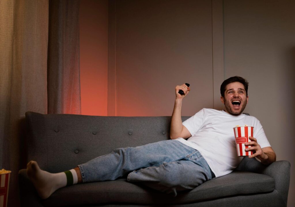 Man laughing while watching TV with popcorn on a couch